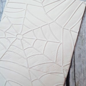 Könnte beinhalten: Weiße Fondant-Platte mit einem geprägten Spinnennetz-Design. Die Platte ist perfekt zum Dekorieren von Kuchen und Cupcakes.