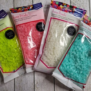 May include: Four bags of fuse beads, each containing 1100 pieces. The bags are labeled "Fuse Beads" and show the beads in different colors: green, pink, white, and blue.