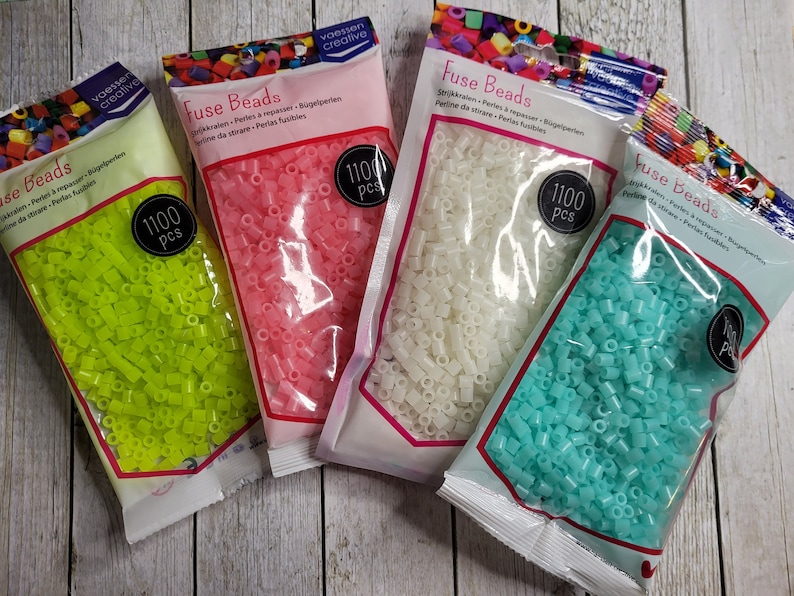 May include: Four bags of fuse beads, each containing 1100 pieces. The bags are labeled "Fuse Beads" and show the beads in different colors: green, pink, white, and blue.
