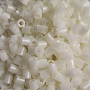 May include: A close-up image of a pile of white plastic beads. The beads are small and round, with a hole in the center. They are perfect for crafting and jewelry making.