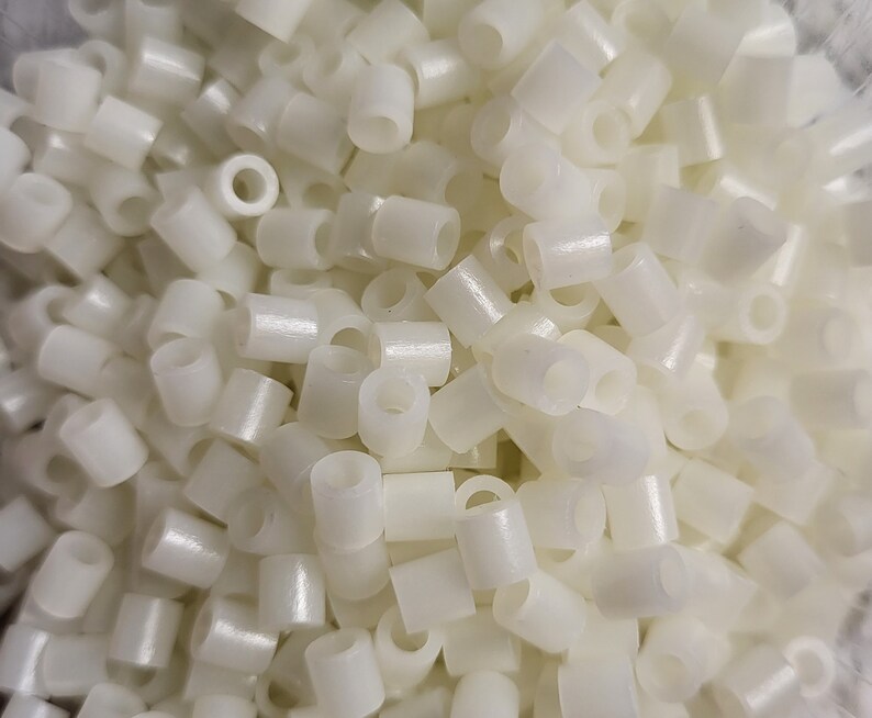 May include: A close-up image of a pile of white plastic beads. The beads are small and round, with a hole in the center. They are perfect for crafting and jewelry making.