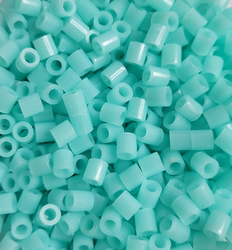 May include: A close-up of a pile of turquoise plastic beads. The beads are small and cylindrical, with a hole in the center. They are perfect for crafting projects.