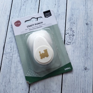 May include: A white craft punch with a gold train design. The packaging says "Craft Punch" and "Small".