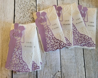 May include: Five white wedding invitation cards with a purple silhouette of a bride and groom. The cards have a lace-like design and the text "L & R 08. Juni 2024" printed on them.