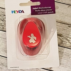 Könnte beinhalten: Roter Kunststoff-Motivstanzer mit Hebel. Der Stanzer ist zum Ausstanzen einer Engelform. Die Verpackung enthält den Markennamen Heyda und den Text "Hebe-Motivstanzer, Perfo-déco à levier, Lever craft punch".
