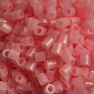May include: A large pile of pink plastic beads. The beads are small and round with a hole in the center.