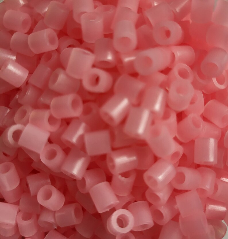 May include: A large pile of pink plastic beads. The beads are small and round with a hole in the center.
