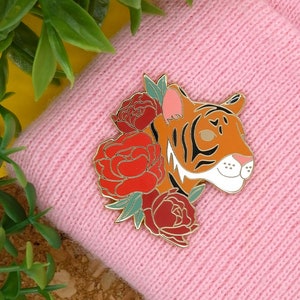May include: Gold-tone enamel pin featuring a tiger's head with black stripes and a red, green, and gold floral design.