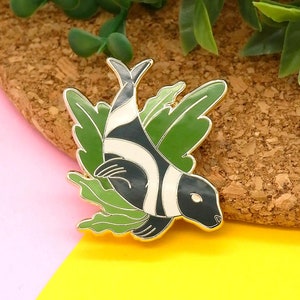 May include: Gold-tone enamel pin featuring a black and white striped fish swimming through green seaweed.