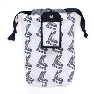 May include: A white drawstring bag with a black and white ice skate print. The bag has a black felt tag with a white ice skate print and the word "Skate" on it.