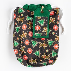 May include: A green drawstring bag with a gingerbread man and Christmas tree pattern. The bag has a green felt tag with a similar pattern.