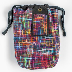 Puede incluir: Una bolsa de cordón negro con un patrón abstracto colorido y una etiqueta negra con un ojal dorado.