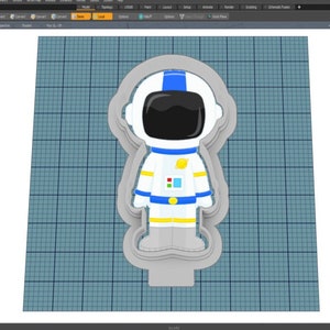 Puede incluir: Un modelo 3D de un cortador de galletas con forma de astronauta. El astronauta lleva un traje espacial blanco con una franja azul en el pecho y una franja amarilla en cada pierna. El astronauta tiene un casco azul con una visera negra.