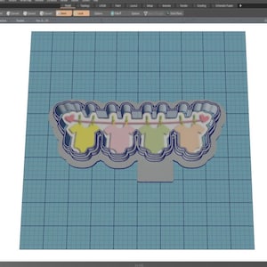 May include: A 3D model of a cookie cutter shaped like a clothesline with four baby onesies hanging on it. The onesies are yellow, pink, green, and orange.