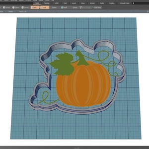 May include: A 3D model of a pumpkin cookie cutter with a green leaf and vine. The cutter is made of metal and has a light gray color.