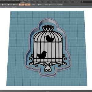 May include: A black metal cookie cutter in the shape of a birdcage with two birds inside. The cutter is on a blue grid background.
