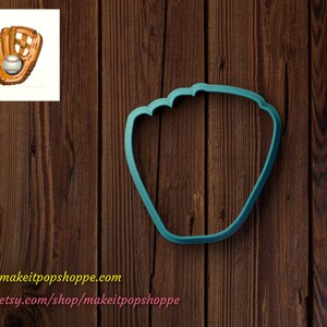 May include: A teal blue plastic cookie cutter shaped like a baseball glove. The cookie cutter is on a brown wooden background.