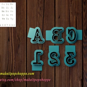 May include: A set of six blue plastic cookie cutters shaped like the letters A, B, C, I, S, and E. The cutters are arranged in two rows on a wooden surface. The text "www.makeitpopshoppe.com" and "www.etsy.com/shop/makeitpopshoppe" is visible at the bottom of the image.