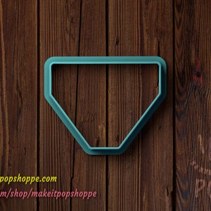 May include: A teal blue plastic cookie cutter shaped like a diamond. The cookie cutter is on a brown wooden background.