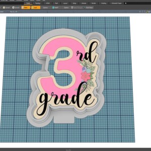 Puede incluir: Un cortador de galletas para 3er grado, con un número 3 rosa y las palabras "3rd grade" en una fuente cursiva. El número 3 tiene un diseño floral. El cortador es de color gris claro.