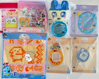 May include: A collection of colorful Tamagotchi merchandise, including plush toys, keychains, stickers, and towels. The items feature various characters and designs, with text in Japanese. The items are packaged in plastic.