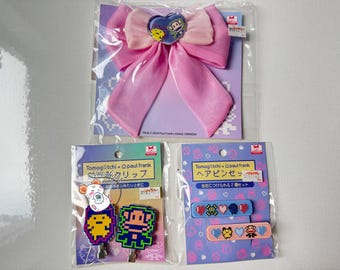 May include: A collection of Paul Frank hair accessories, including a large pink bow with a heart-shaped embellishment and two sets of hair clips. The clips feature pixelated designs of characters and are packaged on purple cards.