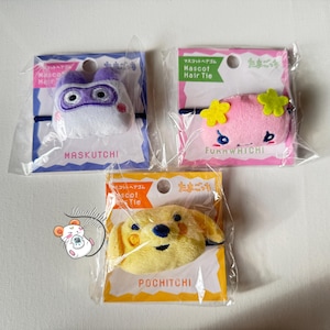 May include: Three mascot hair ties in clear packaging. The top left features a white and purple character with the text "MASKUTCHI". The top right shows a pink character with yellow flowers and the text "FunnWHICHI". The bottom shows a yellow dog with the text "POCHITCHI".