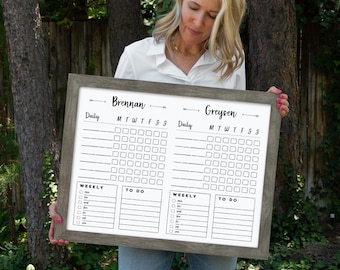 May include: A white dry-erase board with a wooden frame. The board is divided into two sections, each with a daily and weekly checklist. The top of each section has a name, "Brennan" and "Greysen".