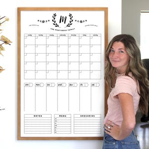 K&ouml;nnte beinhalten: Ein wei&szlig;er, gerahmter Monatskalender mit einem schwarz-wei&szlig;en Design. Der Kalender hat einen Bereich f&uuml;r Notizen, Men&uuml; und Eink&auml;ufe. Oben auf dem Kalender befindet sich ein Kranz mit dem Buchstaben "M" in der Mitte und dem Text "The Martineau Family".
