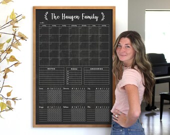 May include: A black chalkboard with a wooden frame and white text that reads "The Haugen Family". The chalkboard is divided into sections for a monthly calendar, notes, menu, and groceries. There are also sections for daily tracking with columns for each day of the week.