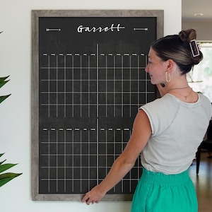 May include: A black chalkboard with a gray wood frame and the name "Garrett" written in white. The chalkboard is divided into a grid of squares, perfect for planning and organizing.