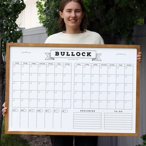 May include: A large, rectangular wooden-framed whiteboard calendar with a white surface. The calendar features a grid layout for monthly planning, with sections for groceries and to-do lists. The word "BULLOCK" is displayed at the top.