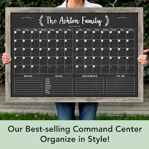 May include: A black chalkboard with a wooden frame and a white calendar grid. The calendar is divided into two sections, each with a month's worth of days. The top of the board has the text "The Ashton Family Established 2018" and a decorative wreath. Below the calendar are sections for notes, menu, groceries, and to do.