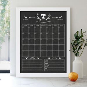 May include: White framed chalkboard with a black background. The chalkboard has a monthly calendar, a notes section, and a menu section. The top of the chalkboard has a white silhouette of a deer head with antlers and the text "The Thompson Family".