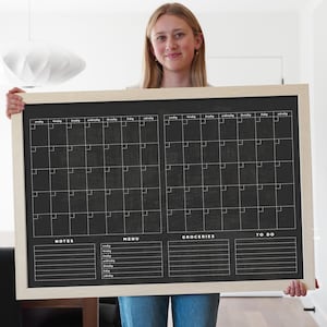 May include: A black chalkboard with a white frame, divided into four sections. The top two sections are monthly calendars with the days of the week labeled. The bottom two sections are labeled "Notes", "Menu", "Groceries", and "To Do" with blank lines for writing.
