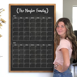 May include: A black chalkboard with a wooden frame and the text "The Naylor Family" in white cursive lettering. The chalkboard is divided into two sections, each with a monthly calendar grid. The calendar grid has the days of the week labeled at the top and the numbers of the month in each square.