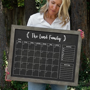 May include: A black chalkboard with a wooden frame, featuring a monthly calendar, a menu section, and a notes section. The chalkboard has the text "The Lund Family" written in white at the top.