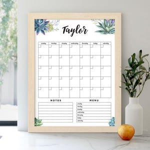 Op de afbeelding: Een witte droog uitwisbare kalender met een houten frame. De kalender heeft een maandelijks raster met vakjes voor elke dag van de week. Bovenaan de kalender staat de naam "Taylor" in zwarte cursieve letters. De kalender heeft ook secties voor notities en een menu.