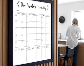 May include: A black framed dry erase calendar with the text "The Walsh Family" at the top. The calendar has a grid of squares for each day of the month, with the days of the week labeled at the top. The calendar is hanging on a wooden wall.