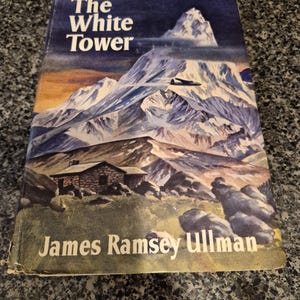 May include: A vintage copy of "The White Tower" by James Ramsey Ullman. The cover depicts a mountain scene with a plane. The title and author's name are in white against a dark blue backdrop.
