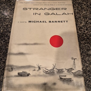 Puede incluir: Una portada de libro vintage titulada "Stranger in Galah" de Michael Barrett. La portada presenta un círculo rojo, un paisaje con un camión, edificios y un molino de viento, y el texto "what happens when a stranger drives into a remote Australian outback town with the body of a murdered aborigine."