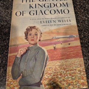 May include: Vintage book cover for "The Gentle Kingdom of Giacomo" by Evelyn Wells. The cover features a woman in a gray shirt standing in a field of flowers. The title is in large, bold letters at the top.