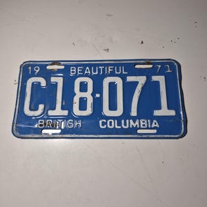 May include: A rectangular blue metal license plate from British Columbia, dated 1971. The plate features white embossed text reading 19, 71, BEAUTIFUL, BRITISH COLUMBIA, and the alphanumeric sequence C18-071, with mounting holes at the top and bottom.