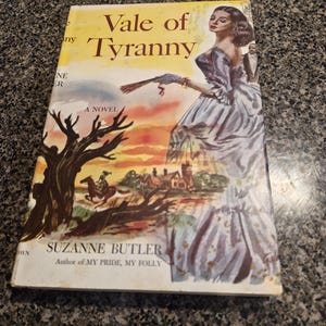 May include: A hardcover book titled Vale of Tyranny by Suzanne Butler. The cover features a colorful illustration of a person in a long blue dress holding a fan, a horse rider, a dark tree, and a building against a yellow and orange sunset sky.