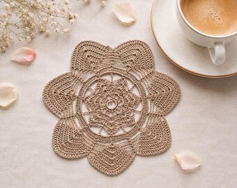 May include: A beige crochet coaster featuring a six-petaled flower design with intricate circular patterns in the center. The piece is crafted from fine thread with a detailed openwork structure, showcasing a symmetrical arrangement of stitches.