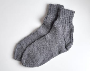 May include: A pair of gray knitted socks. The socks are made of a soft, textured material and have ribbed cuffs. The socks are designed to be worn on the feet and provide warmth and comfort. The socks are a neutral color and can be worn with a variety of outfits.