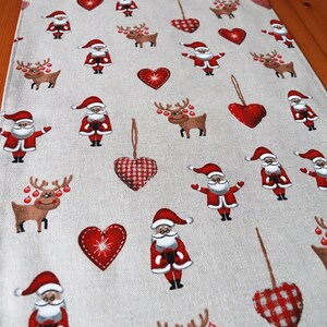 May include: A beige table runner with a repeating pattern of red hearts, reindeer, and Santa Claus figures. The hearts have a checkered pattern.