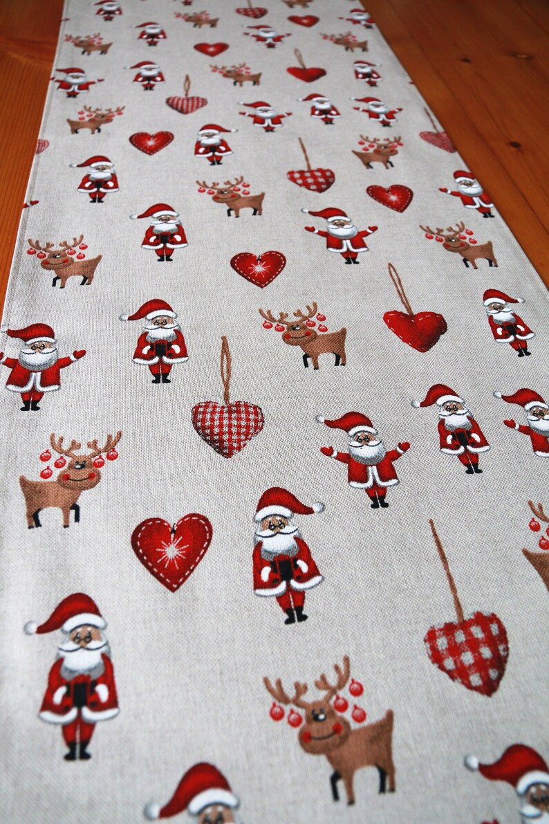 May include: A beige table runner with a repeating pattern of red hearts, reindeer, and Santa Claus figures. The hearts have a checkered pattern.