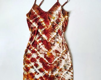 May include: A tie-dye dress with a V-neck and spaghetti straps. The dress features a pattern of red, white, and brown hues. The dress is a bodycon style and appears to be made of a soft, stretchy material.