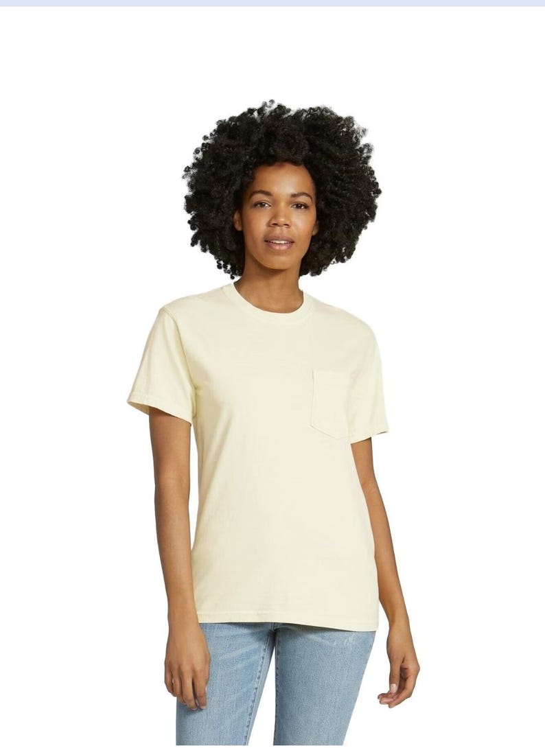 K&ouml;nnte beinhalten: Ein hellgelbes T-Shirt mit Brusttasche. Das kurz&auml;rmelige Shirt wird von einer Person mit dunklem, lockigem Haar und einer Jeans getragen. Das Shirt ist aus weichem Material und hat einen klassischen, l&auml;ssigen Stil.